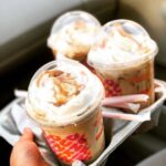 Three iced coffees from Dunkin' in a drink carrier with curved lids and whipped cream on top.